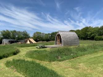 The best camping pod in Cornwall, in front of a blue sky with fire pit area in back
