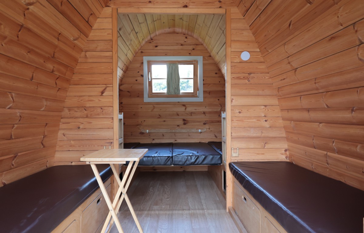 Inside a timber camping pod showing the kingsize bed at back and two kids' bench beds in foreground