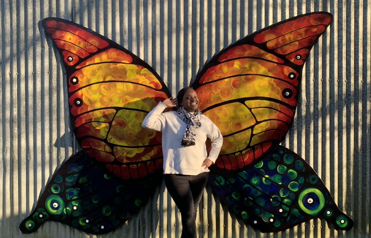 A smiling black woman poses in front of the huge colourful butterfly wings at the barn