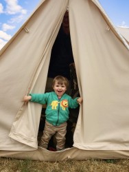 A happy smiling toddler opens the canvas door to a bell tent.